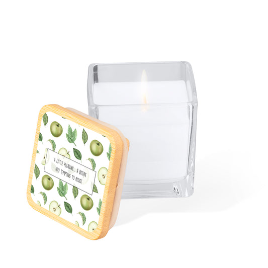 Vela aromática en tarro de cristal cuadrado con tapa de bambú. Diseño impreso: fondo color blanco con manzanas verdes y hojas estilo acuarela. En el centro un rectángulo blanco con la frase: "A little pleasure... a desire too tempting to resist"