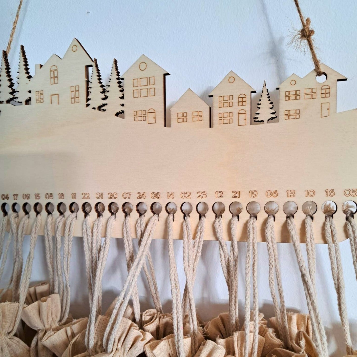 Detalle del calendario de adviento de madera en forma de pueblo invernal, con los 24 agujeros y sus saquitos colgando preparados para rellenar con sorpresas.