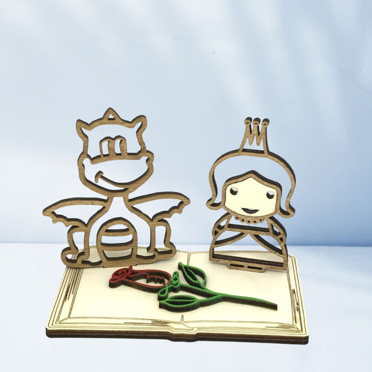 Figura decorativa de madera con la princesa y el dragón de Sant Jordi sobre una base en forma de libro y una rosa, pieza artesanal sostenible ideal para regalar o decorar en la Diada de Sant Jordi.
