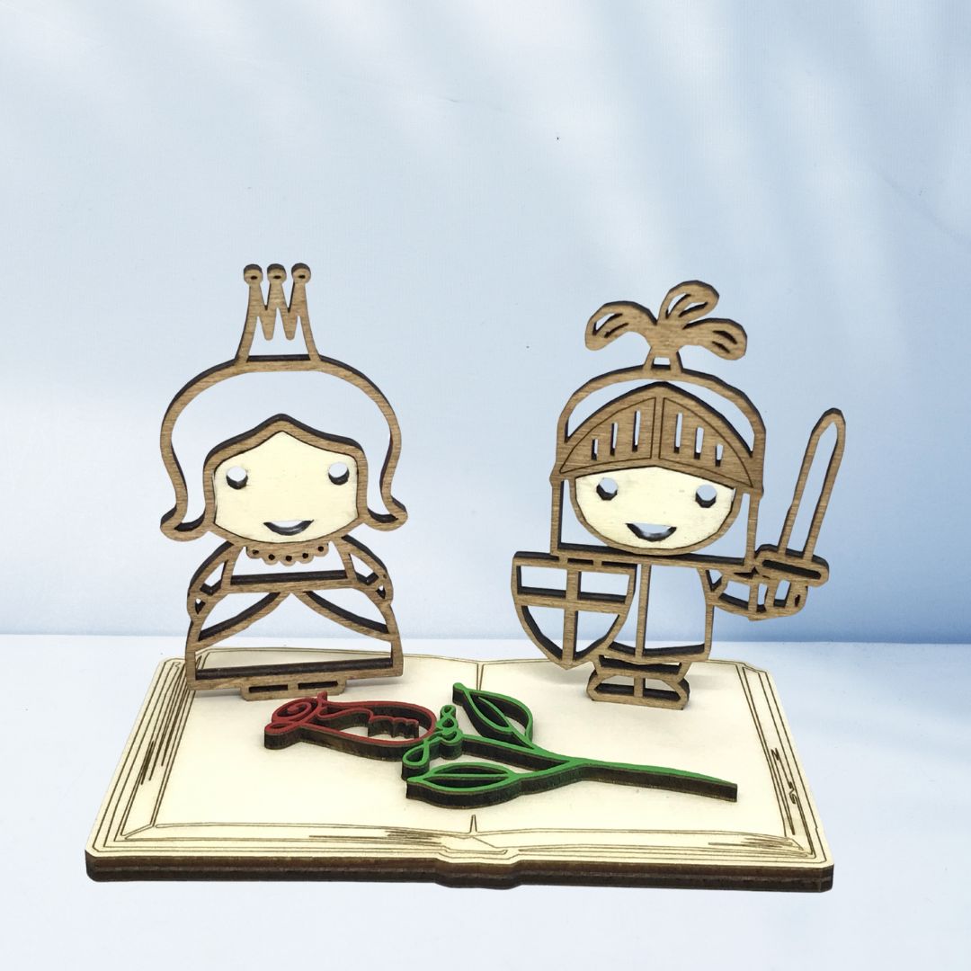 Figura decorativa de madera con el caballero y la princesa de Sant Jordi sobre una base en forma de libro y una rosa, pieza artesanal sostenible ideal para regalar o decorar en la Diada de Sant Jordi.