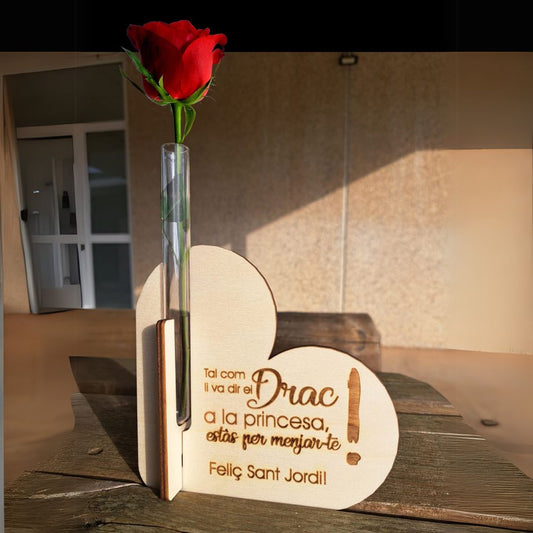 Porta rosas de madera formado por dos corazones cruzados y un tubo de cristal para poner la rosa con agua. Personalizado con una frase de amor grabada a láser en la madera especial para Sant Jordi. Frase: Tal com li va dir el drac a la princesa: estàs per menjar-te! Feliç Sant Jordi"