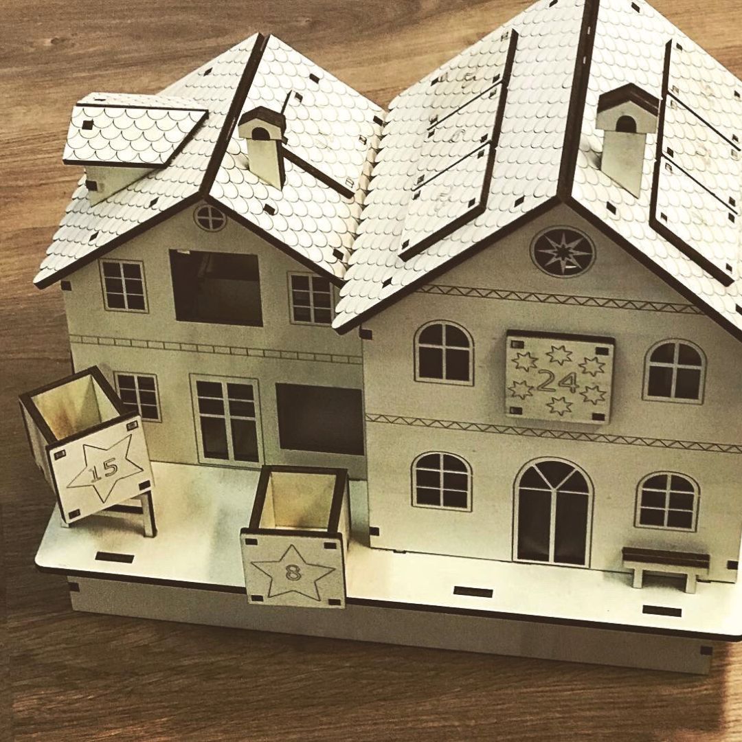 Calendario de adviento de madera en forma de casa con distintos compartimentos de madera estilo cajón donde guardar la sorpresa de cada día