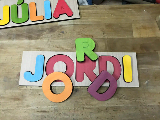 Juego infantil de madera para encajar letras. Personalizado con el nombre del niño o niña, las letras se pintan aleatoriamente para que combinen en conjunto.