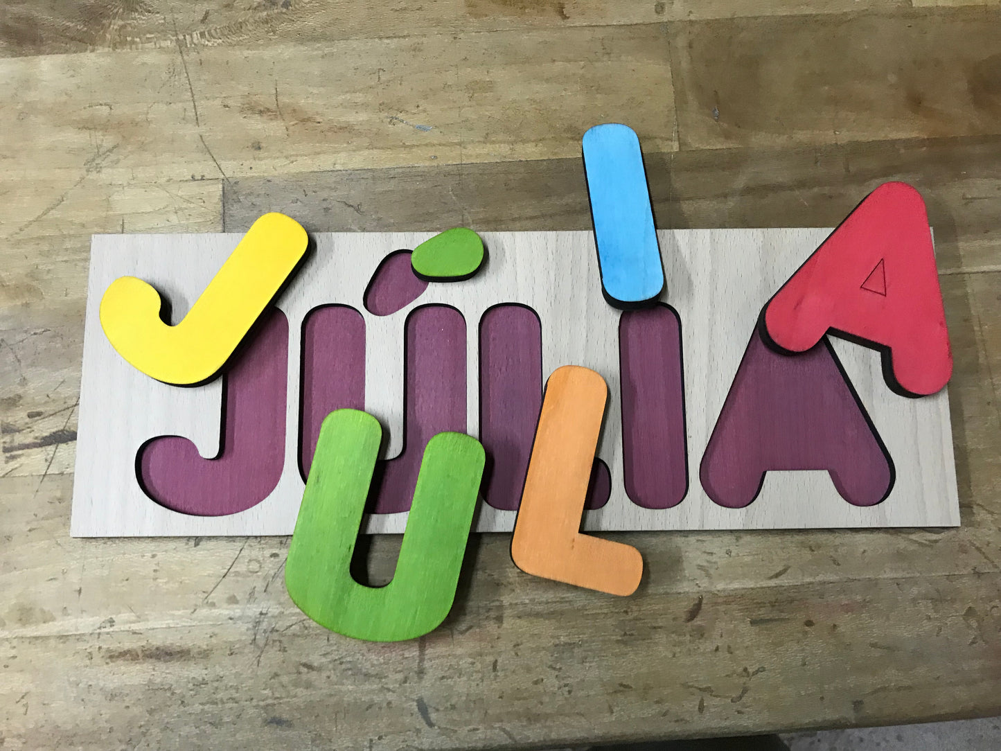 Juego infantil de madera para encajar letras. Personalizado con el nombre del niño o niña, las letras se pintan aleatoriamente para que combinen en conjunto.