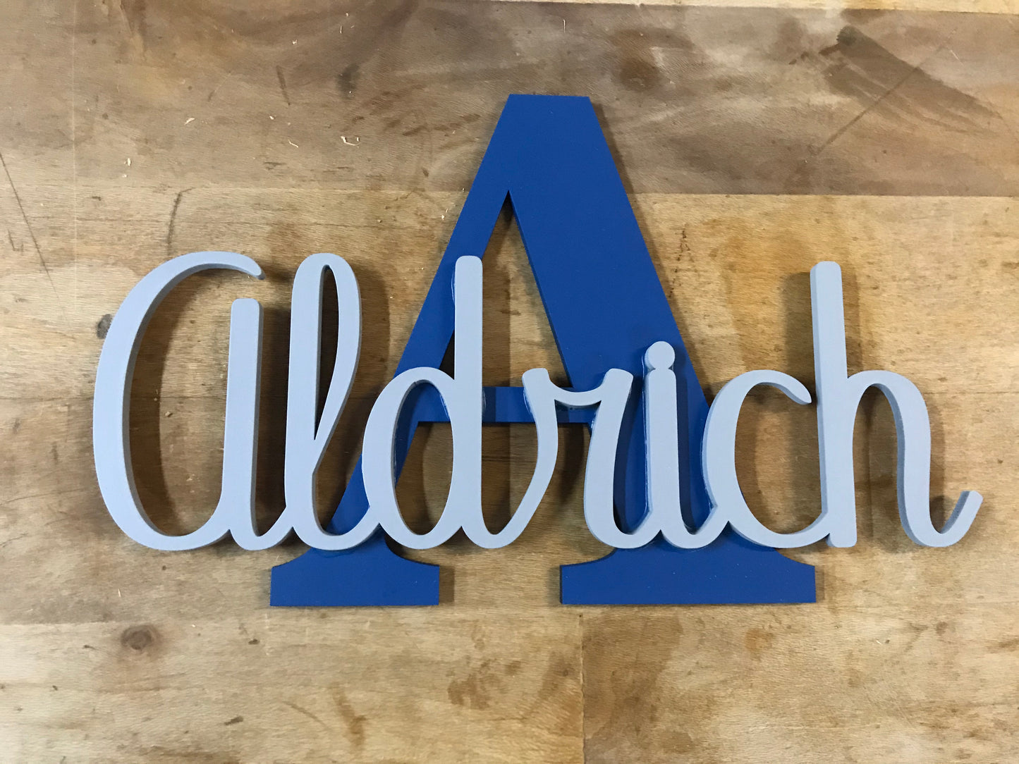 Nombre decorativo de madera, troquelado y montado sobre inicial de madera de chopo pintadas a dos colores para mayor contraste. Combinación de dos azules