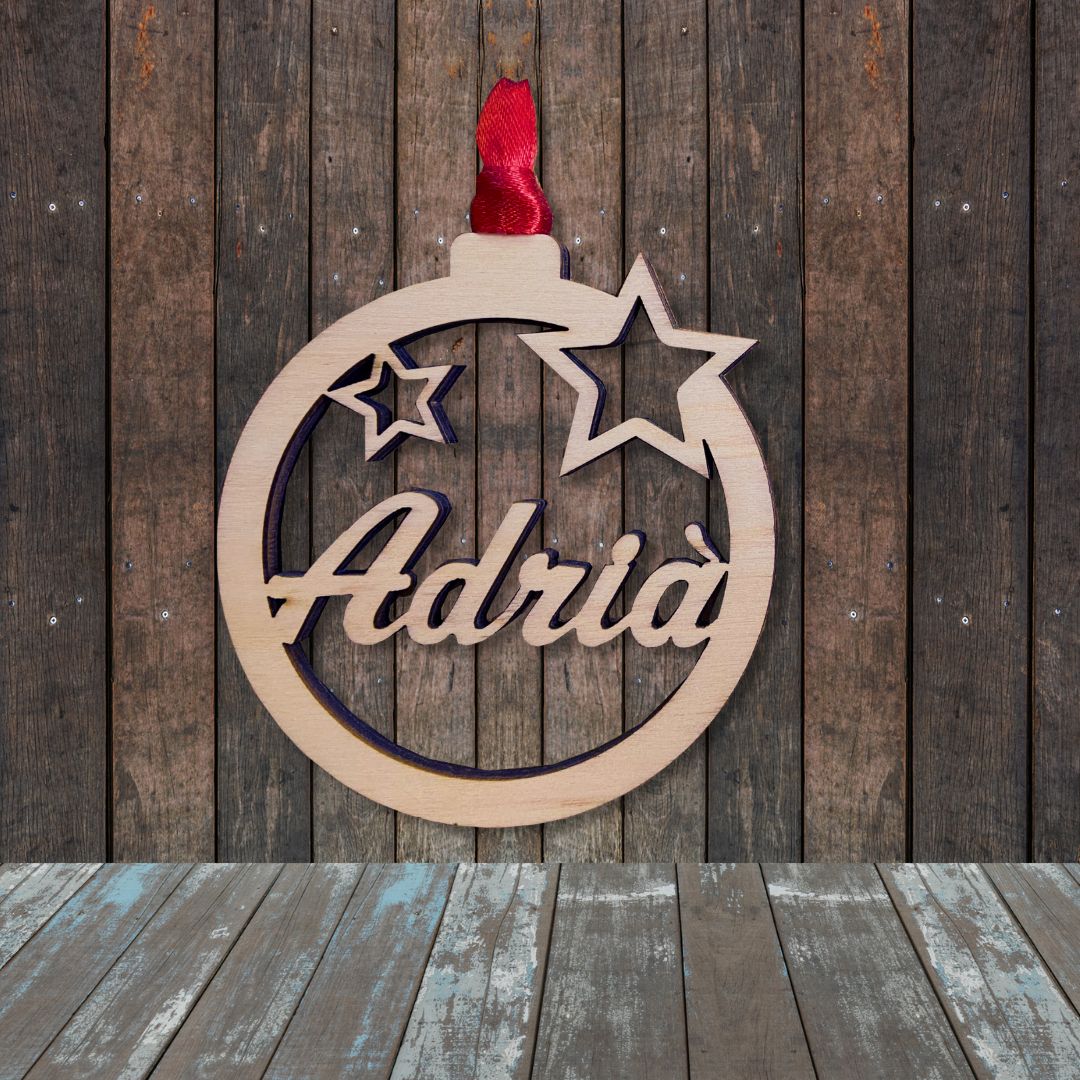 Bola de navidad de madera formada por un círculo y dos estrellas troqueladas y el nombre en el centro. Ligera y resistente. Incluye cinta roja para colgar en el árbol.