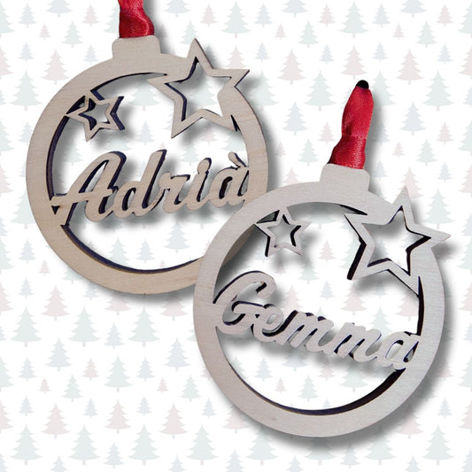 Bola de navidad de madera formada por un círculo y dos estrellas troqueladas y el nombre en el centro. Ligera y resistente. Incluye cinta roja para colgar en el árbol.