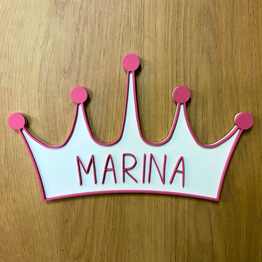 Corona de madera con cinco puntas, detalle en relieve y color en el contorno de la pieza. Personalizada con el nombre de la reina de la casa a conjunto con el relieve. Ejemplo en color rosa.