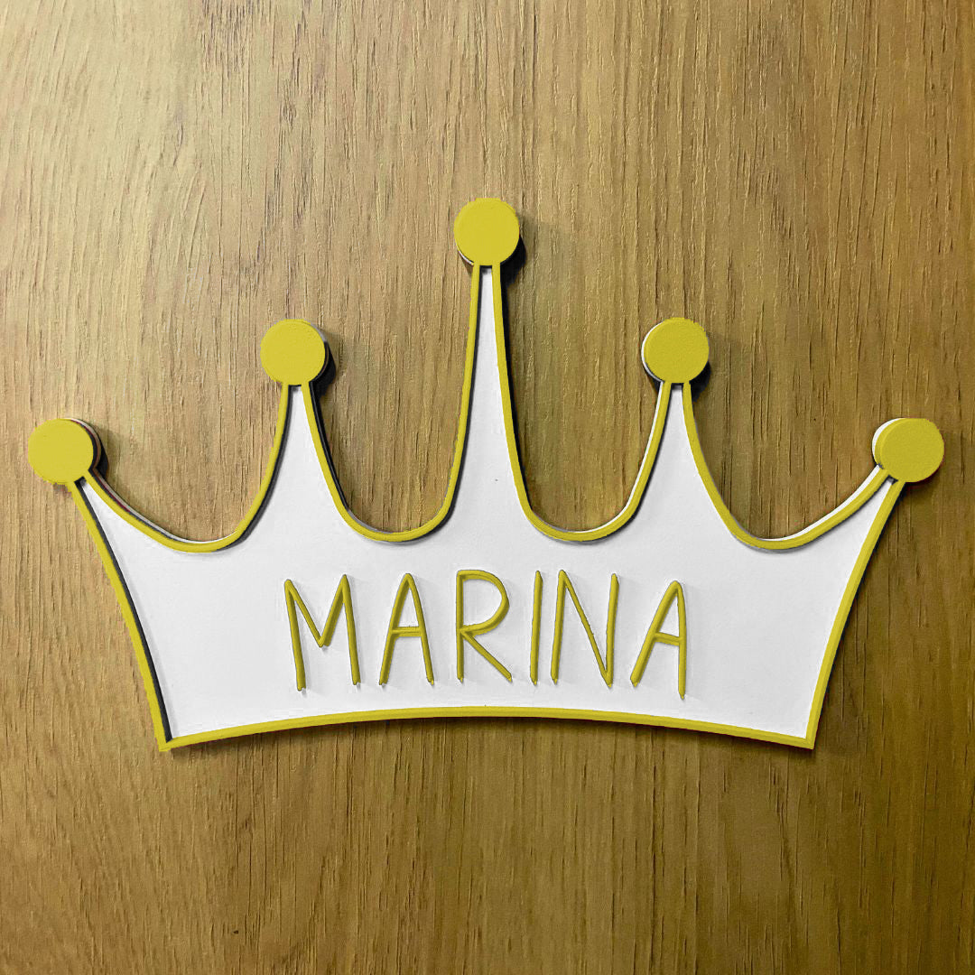 Corona de madera con cinco puntas, detalle en relieve y color en el contorno de la pieza. Personalizada con el nombre de la reina de la casa a conjunto con el relieve. Ejemplo en color amarillo.