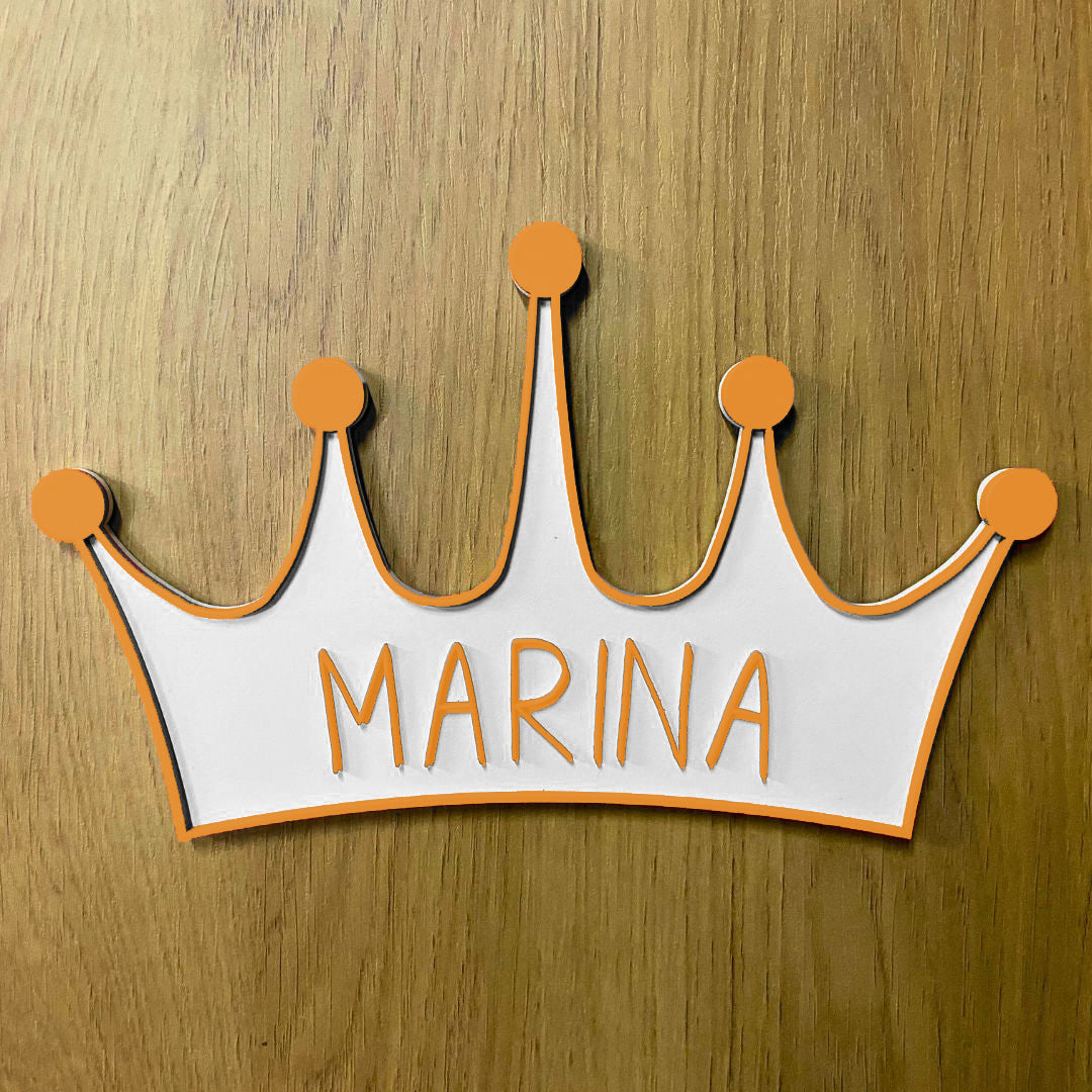 Corona de madera con cinco puntas, detalle en relieve y color en el contorno de la pieza. Personalizada con el nombre de la reina de la casa a conjunto con el relieve. Ejemplo en color naranja.