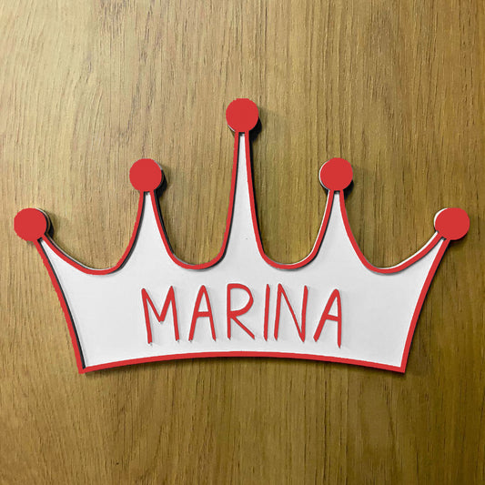 Corona de madera con cinco puntas, detalle en relieve y color en el contorno de la pieza. Personalizada con el nombre de la reina de la casa a conjunto con el relieve. Ejemplo en color rojo.
