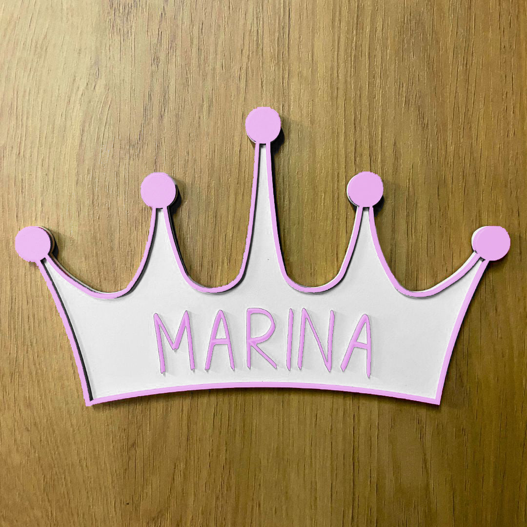 Corona de madera con cinco puntas, detalle en relieve y color en el contorno de la pieza. Personalizada con el nombre de la reina de la casa a conjunto con el relieve. Ejemplo en color morado.