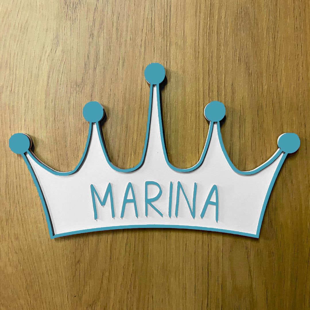 Corona de madera con cinco puntas, detalle en relieve y color en el contorno de la pieza. Personalizada con el nombre de la reina de la casa a conjunto con el relieve. Ejemplo en color azul.