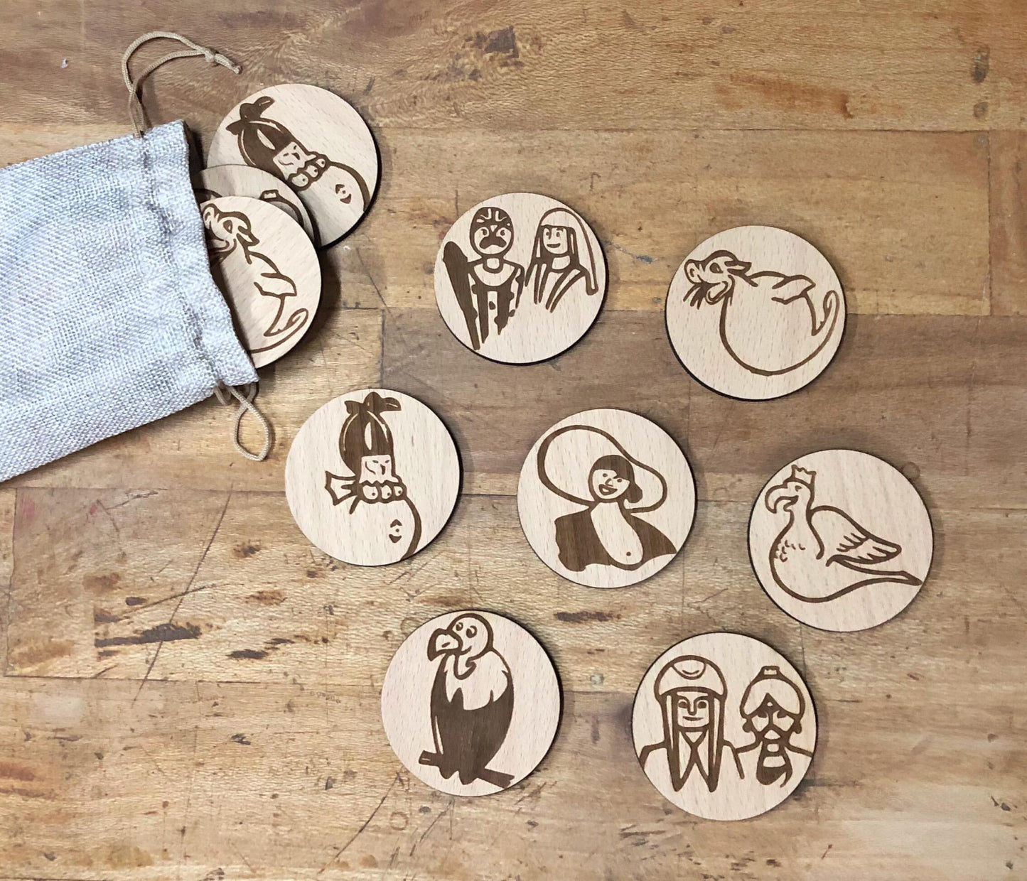 Juego de memoria de madera grabado con personajes y animales populares de La Bisbal, piezas redondas artesanales en bolsa de lino, juguete educativo sostenible y local.