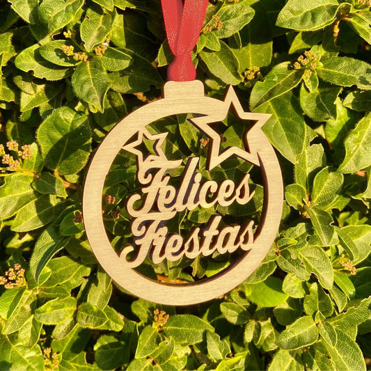 Bola de madera para el árbol de navidad con el mensaje Felices Fiestas troquelado. Incluye cinta roja para colgar del árbol.