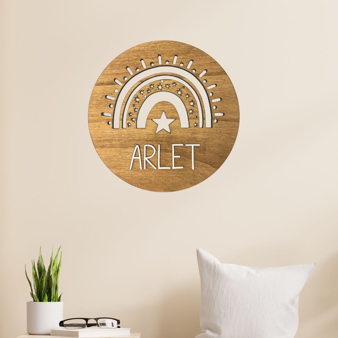 Placa de madera circular para colgar en la pared con detalle de arcoiris troquelado y personalizada con el nombre de la niña o niño en metacrilato blanco.