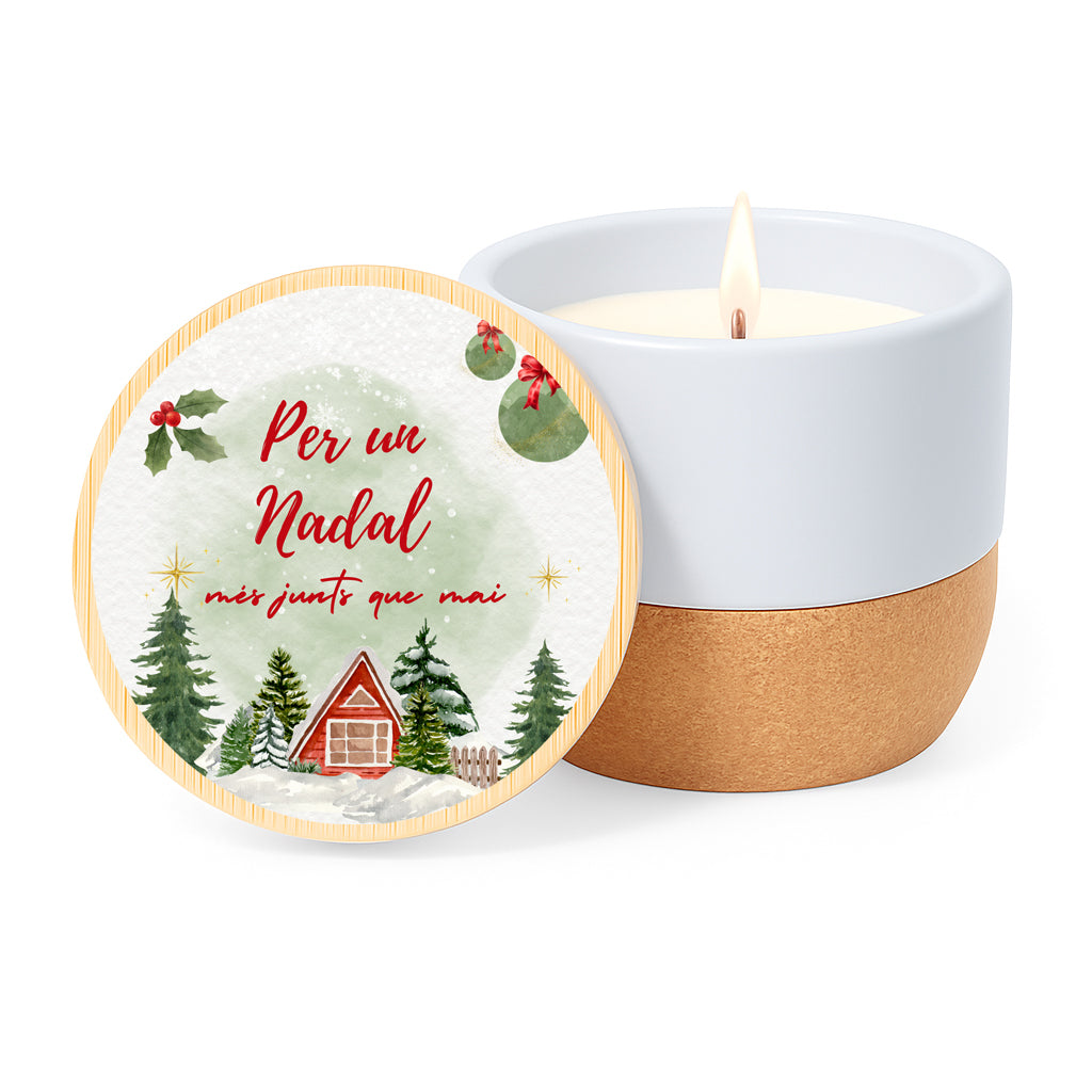 Vela con aroma de lino en tarro de cerámica con base de corcho y tapa de bambú impresa con un diseño de casitas y avetos nevados y la frase Per un Nadal més junts que mai.