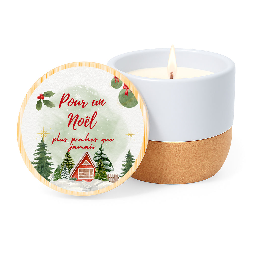 Vela con aroma de lino en tarro de cerámica con base de corcho y tapa de bambú impresa con un diseño de casitas y avetos nevados y la frase Pour un Noël plus proches que jamais.