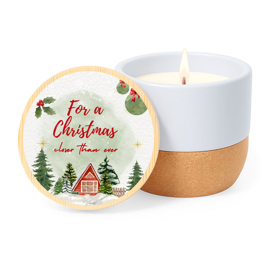 Vela con aroma de lino en tarro de cerámica con base de corcho y tapa de bambú impresa con un diseño de casitas y avetos nevados y la frase For a Christmas closer than ever