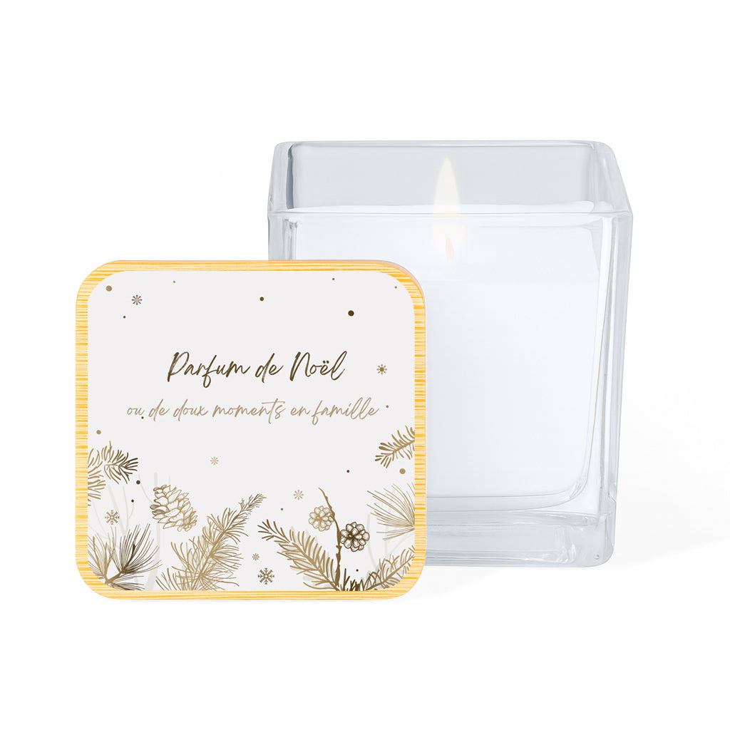 Vela con aroma de vainilla en tarro cuadrado de cristal y tapa de bambú impresa con un diseño navideño de piñas doradas sobre fondo blanco y la frase " Parfum de Noël ou de doux moments en famille"