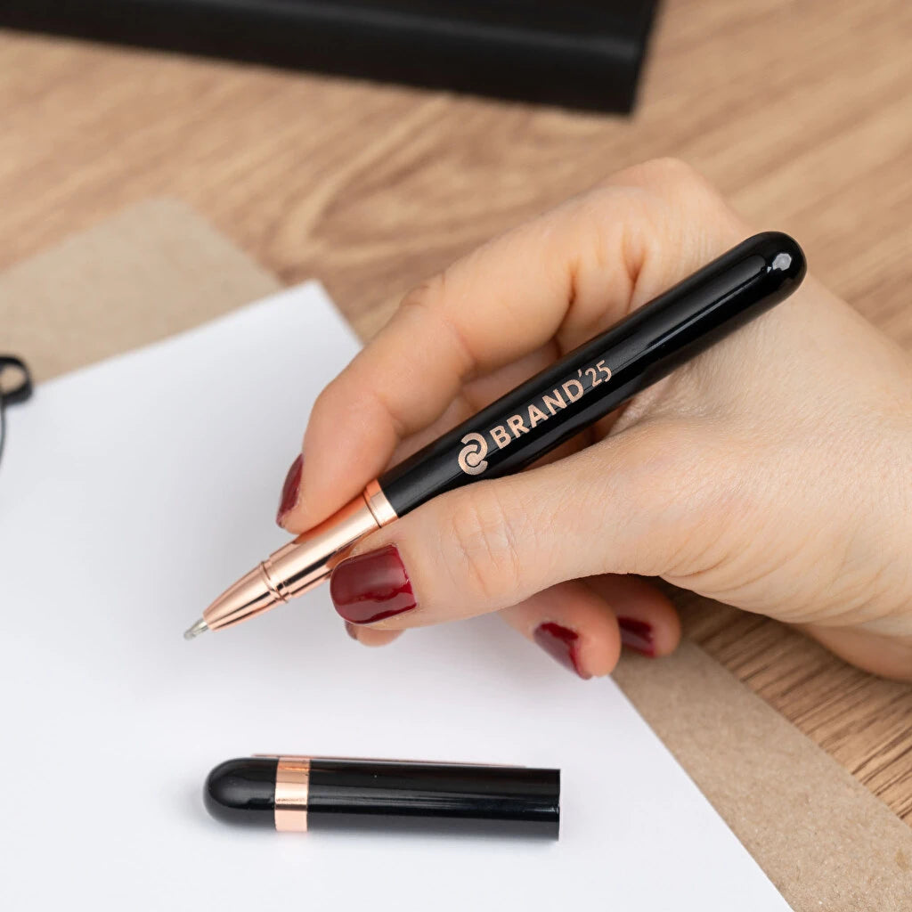 Bolígrafo roller de aluminio con detalles rosados y tinta azul. Color negro. Personalizable con grabado láser. Ideal para regalos elegantes y detalles para eventos.