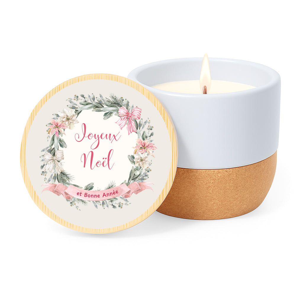 Vela con aroma de lino en tarro de cerámica y base de corcho. Tapa de bambú impresa con diseño clasico de navidad: corona de flores en tonos rosa y la frase Joyex Noel et bonne année