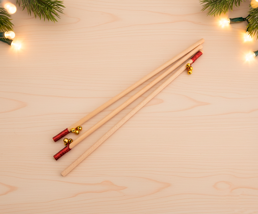 Tres bastones de madera con tres cascabeles dorados cada uno y una cinta roja ornamental a punto de ser personalizados con grabado láser. 