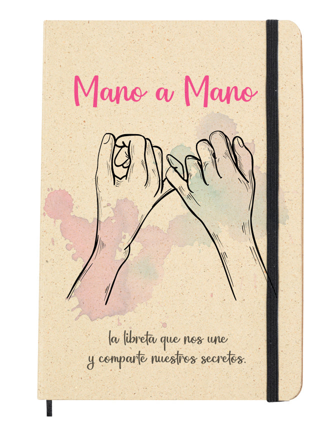 Portada del bloc de notas de hierba reciclada con goma elástica para mantenerla cerrada. Diseño de la portada: Dibujo de dos manos enlazadas por el dedo meñique, con manchas decorativas en rosa y morado.Acompaña la frase "Mano a mano, la libreta que nos une y comparte nuestros secretos.