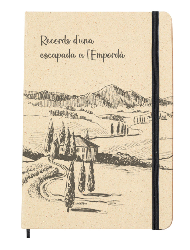 Portada del bloc de notas de hierba reciclada con goma elástica para mantenerla cerrada. Diseño de la portada: paisaje típico de l'Empordà con montañas y campos y una masia catalana como dibujado a mano. Frase con letra manuscrita: "Records d'una escapada a l'Empordà"