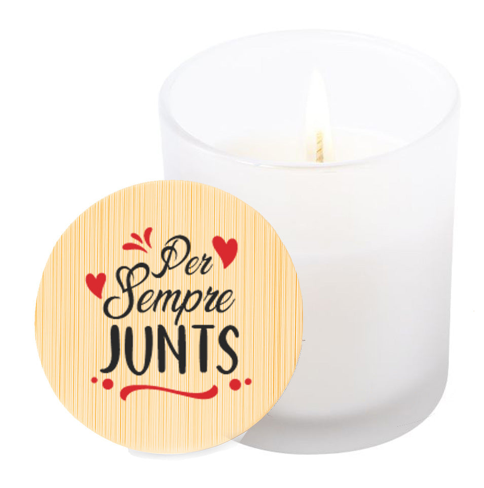 Vela aromática de vainilla en tarro de cristal translúcido con tapa de bambú y mensaje impreso en colores rojo y negro. Per sempre junts