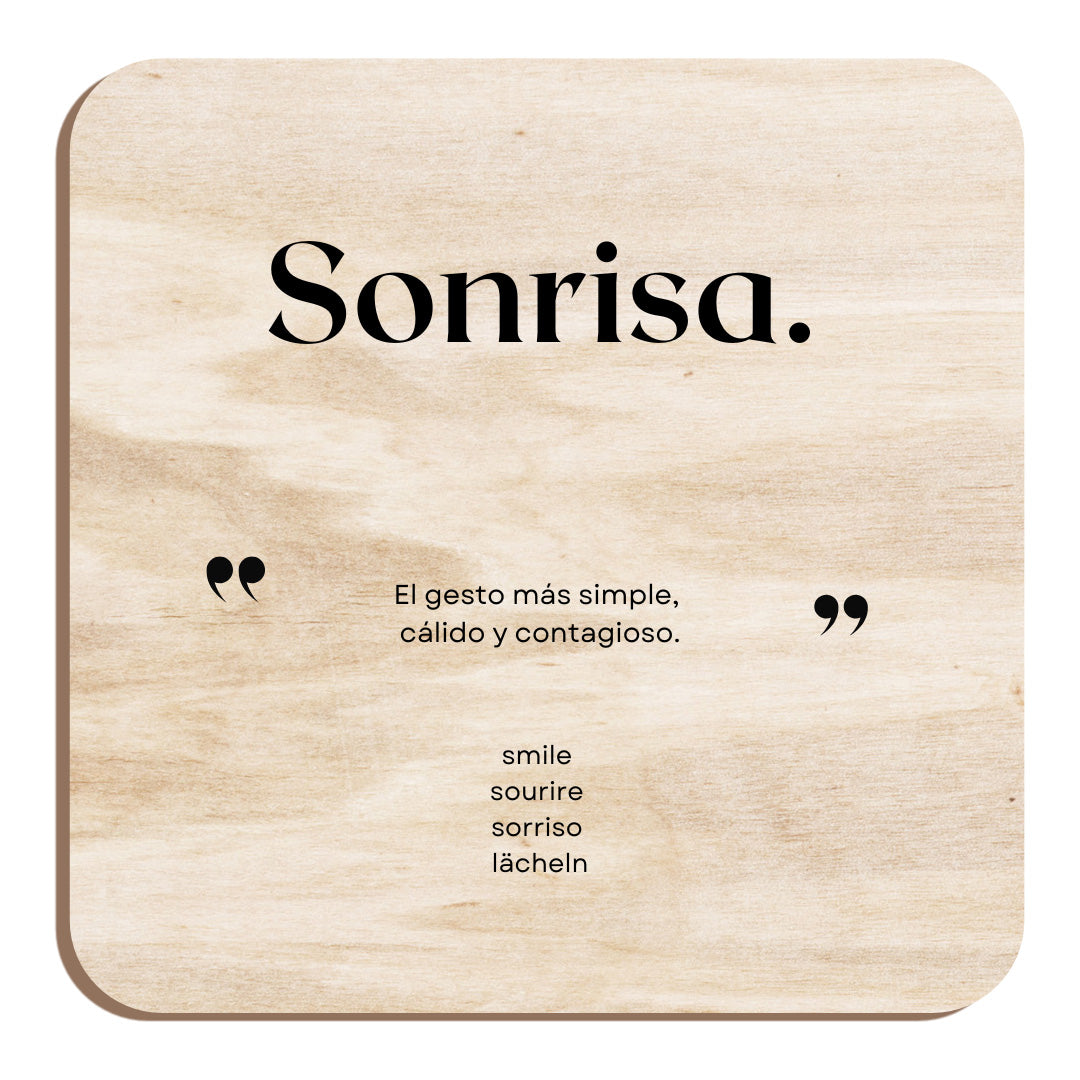 Imán de madera cuadrado que forma parte de la colección Palabras bonitas. Contiene en grande la palabra "Sonrisa" justo debajo entre comillas grandes la descripción "El gesto más simple, cálido y contagioso" y al final la traducción a los cuatro idiomas inglés, francés, italiano y alemán: "Smile / Sourire / Sorriso / Lächeln"