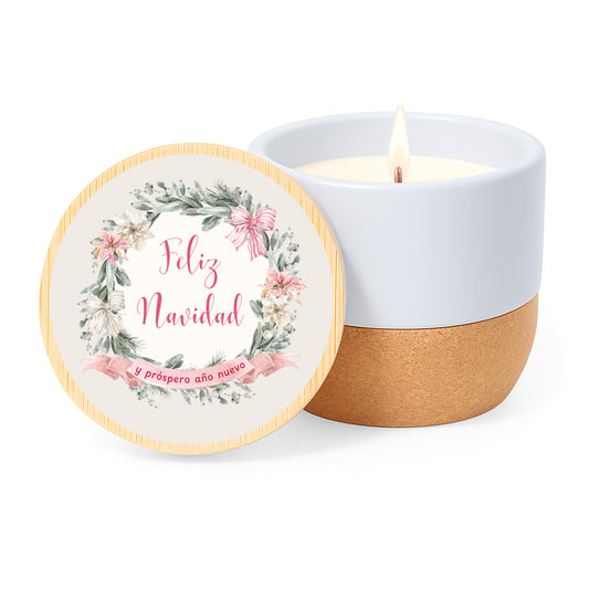Vela con aroma de lino en tarro de cerámica y base de corcho. Tapa de bambú impresa con diseño clasico de navidad: corona de flores en tonos rosa y la frase Feliz Navida y próspero año nuevo