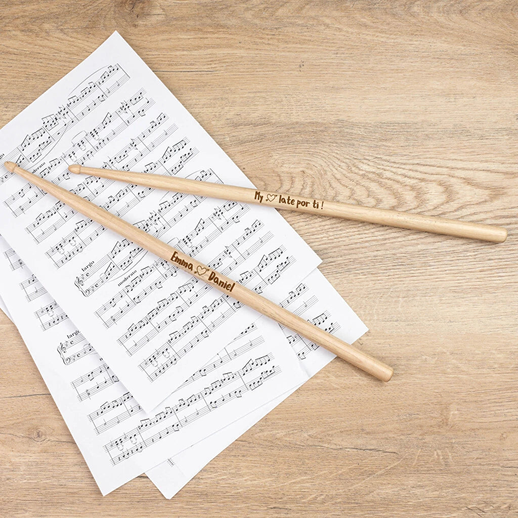 Dos baquetas de batería de madera grabadas a láser sobre una partitura