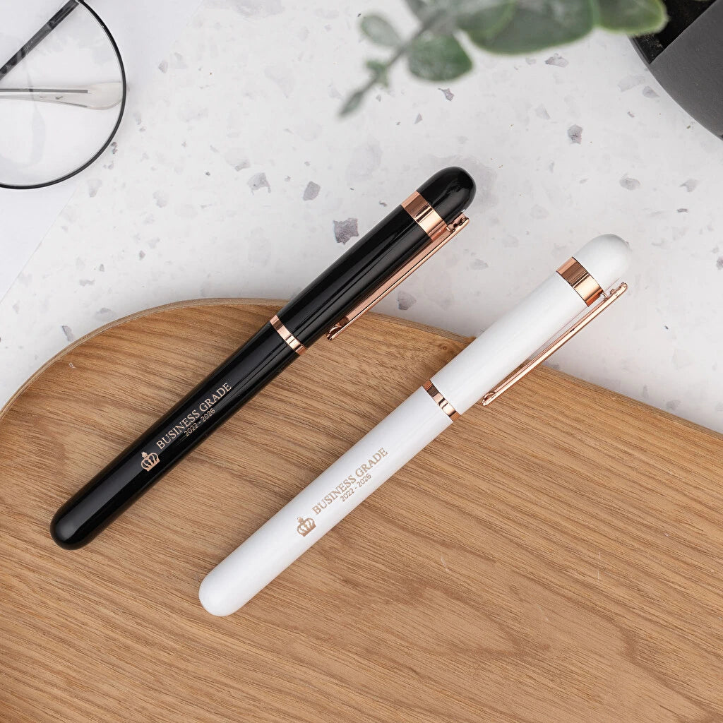 Bolígrafo roller de aluminio con detalles rosados y tinta azul. Color blanco o negro. Personalizable con grabado láser. Ideal para regalos elegantes y detalles para eventos.