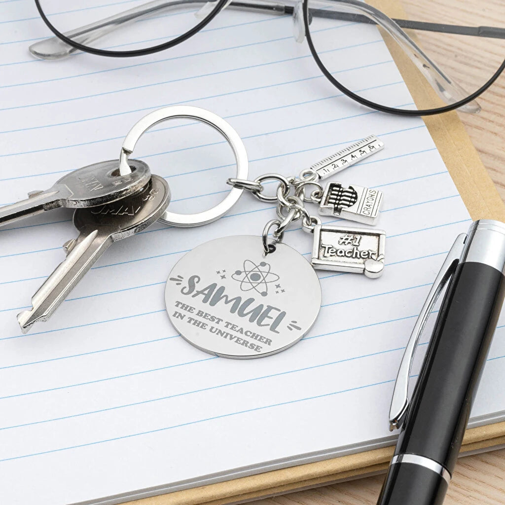 Llavero de acero inoxidable con chapa grabada y charms temáticos: maestros. Personalizable con grabado láser desde 1 unidad. Ideal como regalo original.