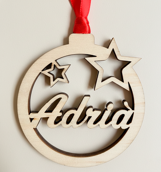 Bola de navidad de madera formada por un círculo y dos estrellas troqueladas y el nombre en el centro. Ligera y resistente. Incluye cinta roja para colgar en el árbol. 
