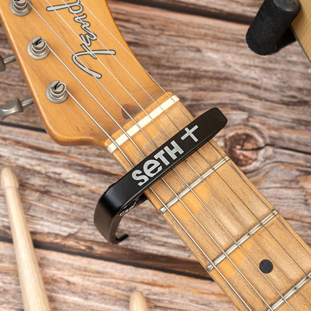 Cejilla de guitarra personalizada con grabado. Fabricada en metal con acolchado protector para el mástil. Acabado metal negro