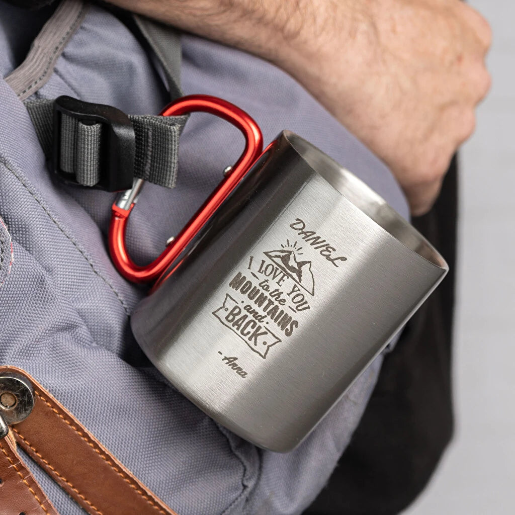 Taza de acero inoxidable con mosquetón y grabado personalizado. Ideal para camping, excursiones y montaña. Resistente, ligera y práctica. Colgada